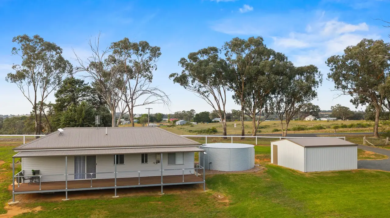 Aerial view of the cottage, round water tank and shed with the town of Young in the distance