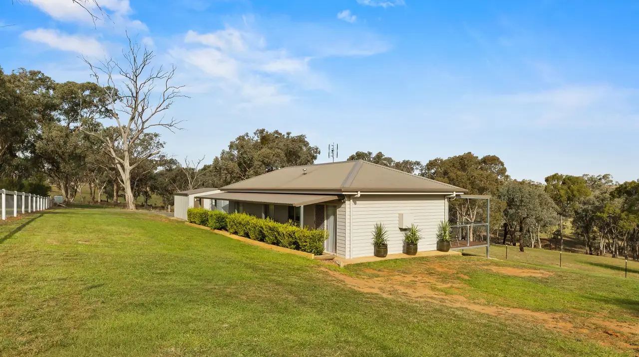 Side of the weatherboard cottage on a sloping green lawn with bushland behind