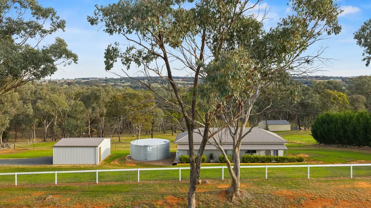 The cottage, water tank and shed seen across a white post-and-rail fence