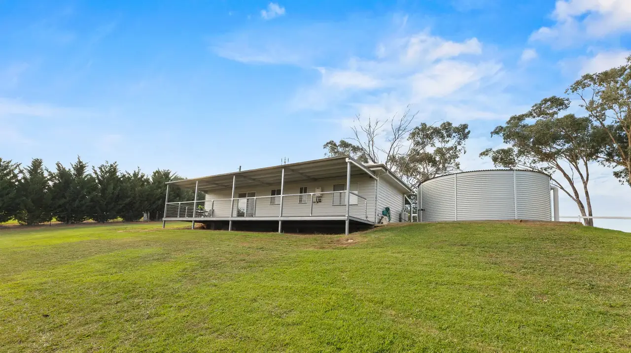 Weatherboard cottage with wraparound verandah beside a large round rainwater tank