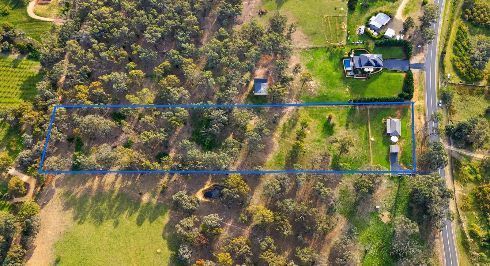 Aerial photograph with the property boundary outlined in blue — cleared paddock at the road end, woodland running west