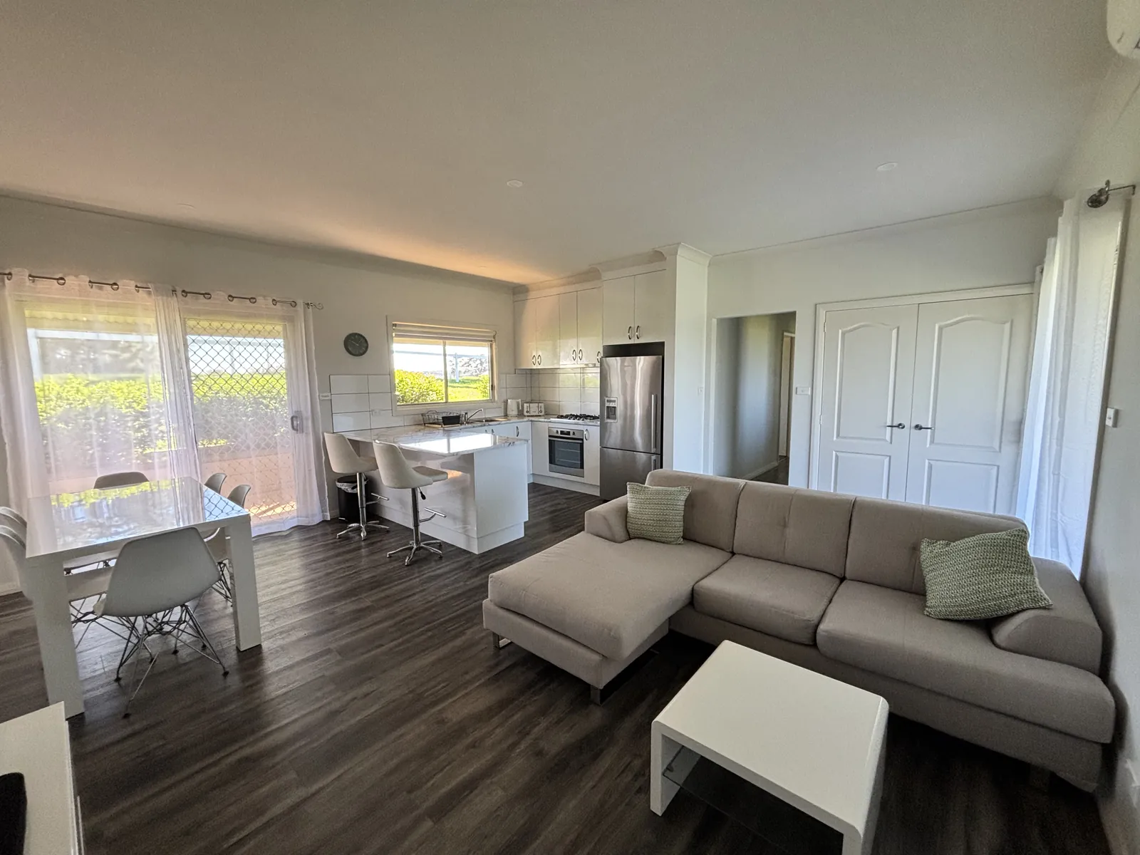 Open-plan living room with a sofa, dining table and white kitchen with stone island bench beyond
