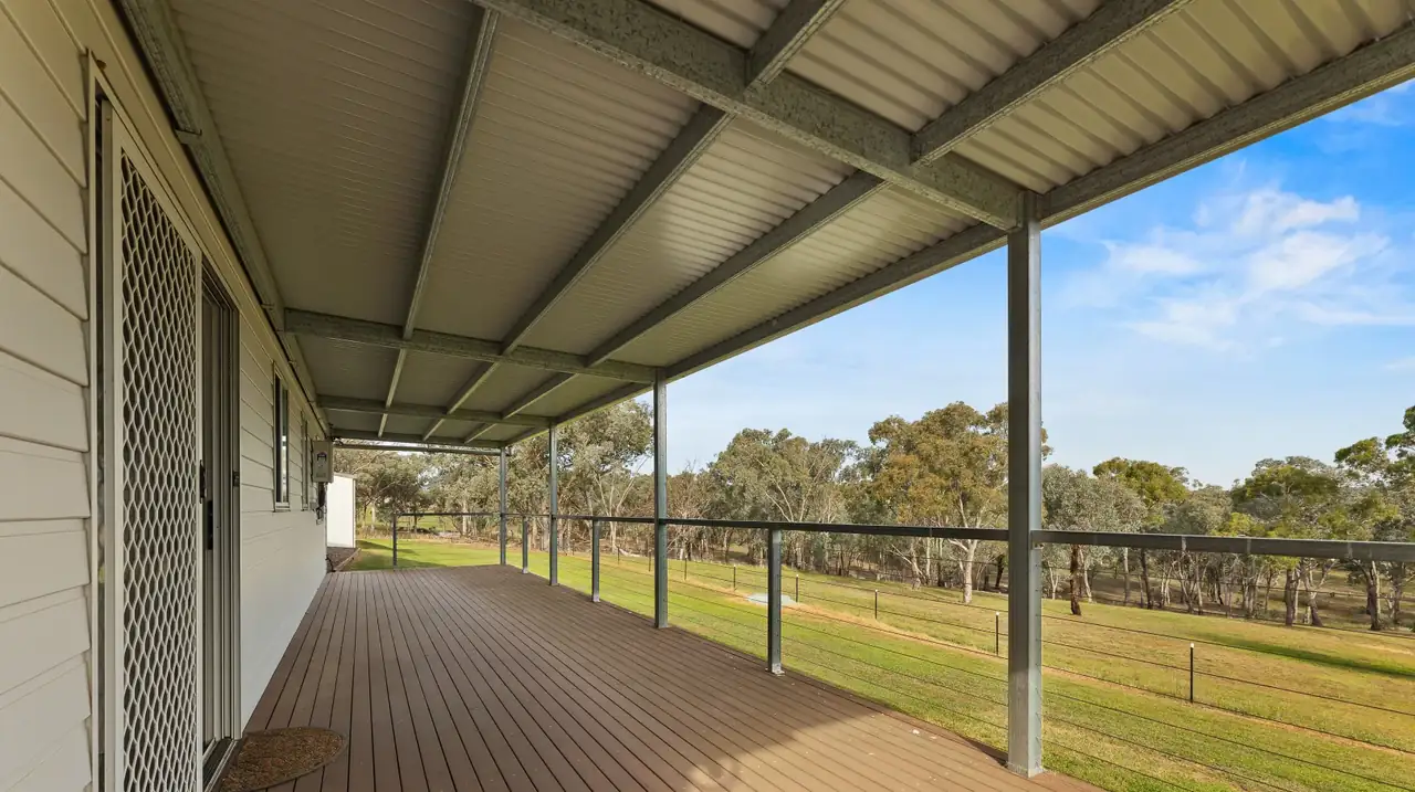 Long covered verandah with wire balustrade looking over green paddock and gum trees