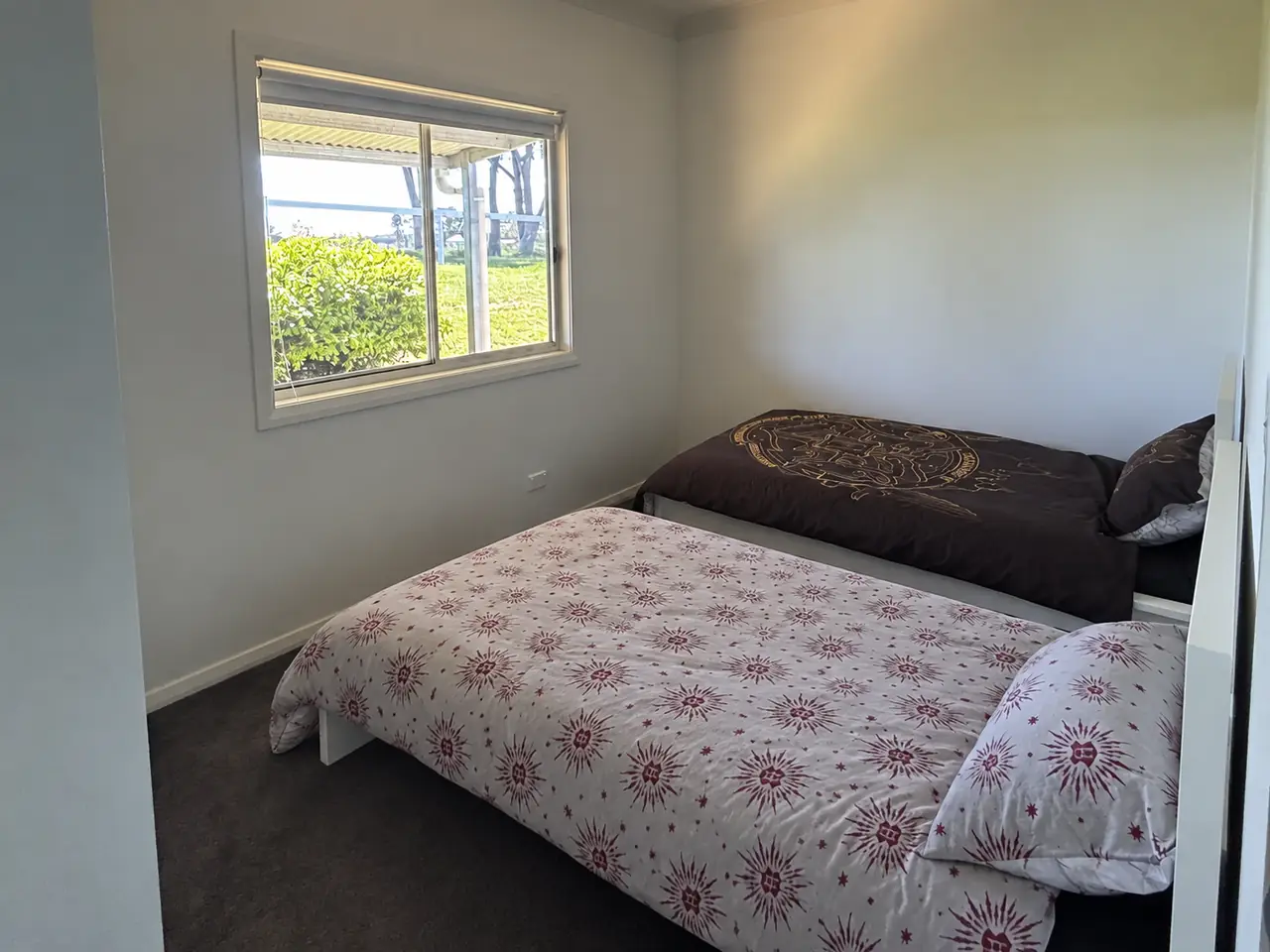 Bedroom with two white single beds and a window looking onto the garden and paddock