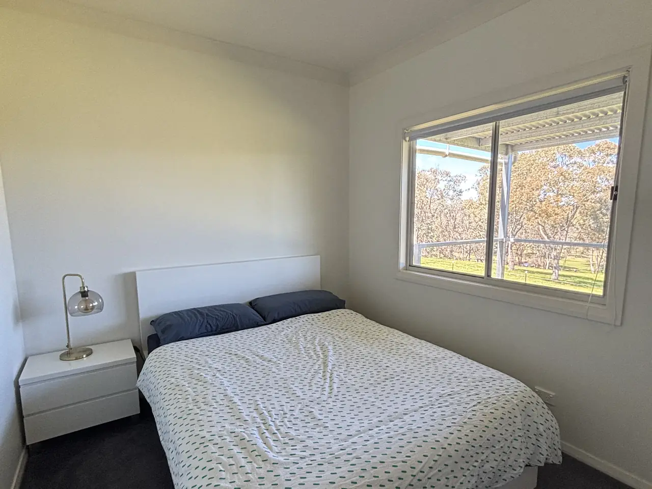 Bedroom with a queen bed, teal throw and a window onto the verandah